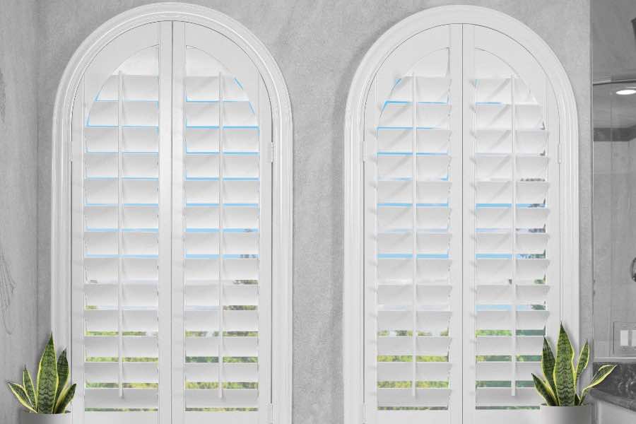 White Polywood shutters on two arched windows by a bathtub